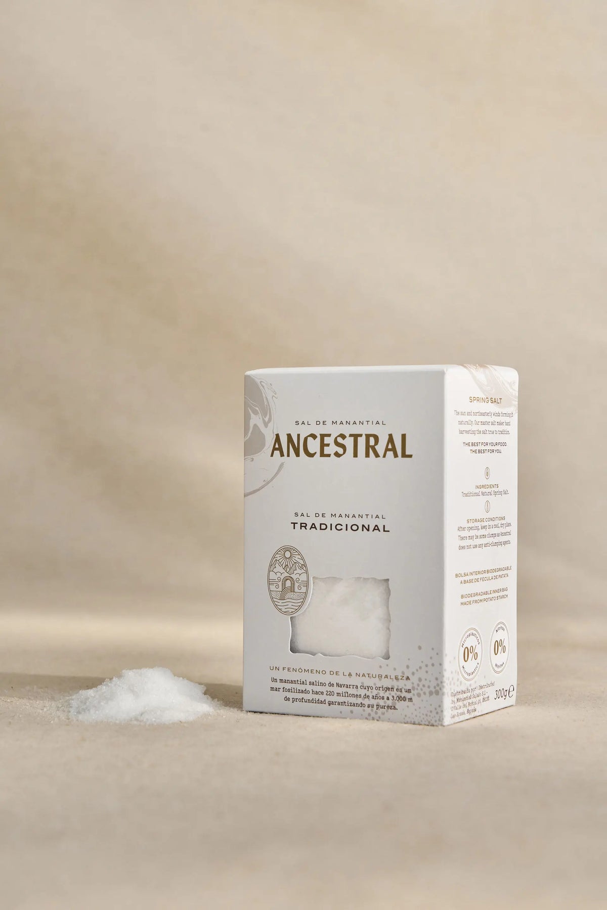 White rectangular box of fine spring salt with a cutout window, next to a small pile of white salt on beige background.