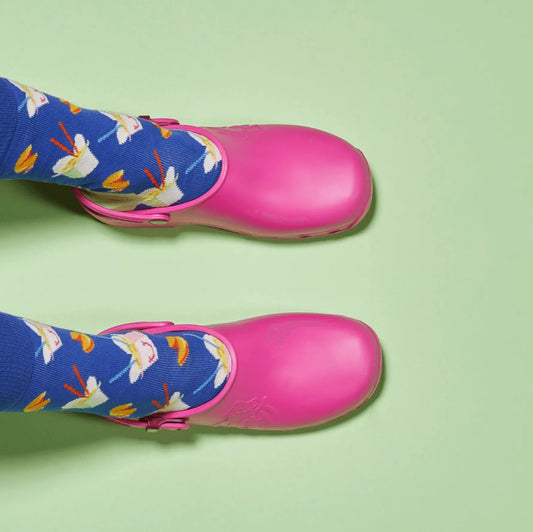 Bright pink rubber clogs worn with blue patterned socks, shown from above against a light green background.