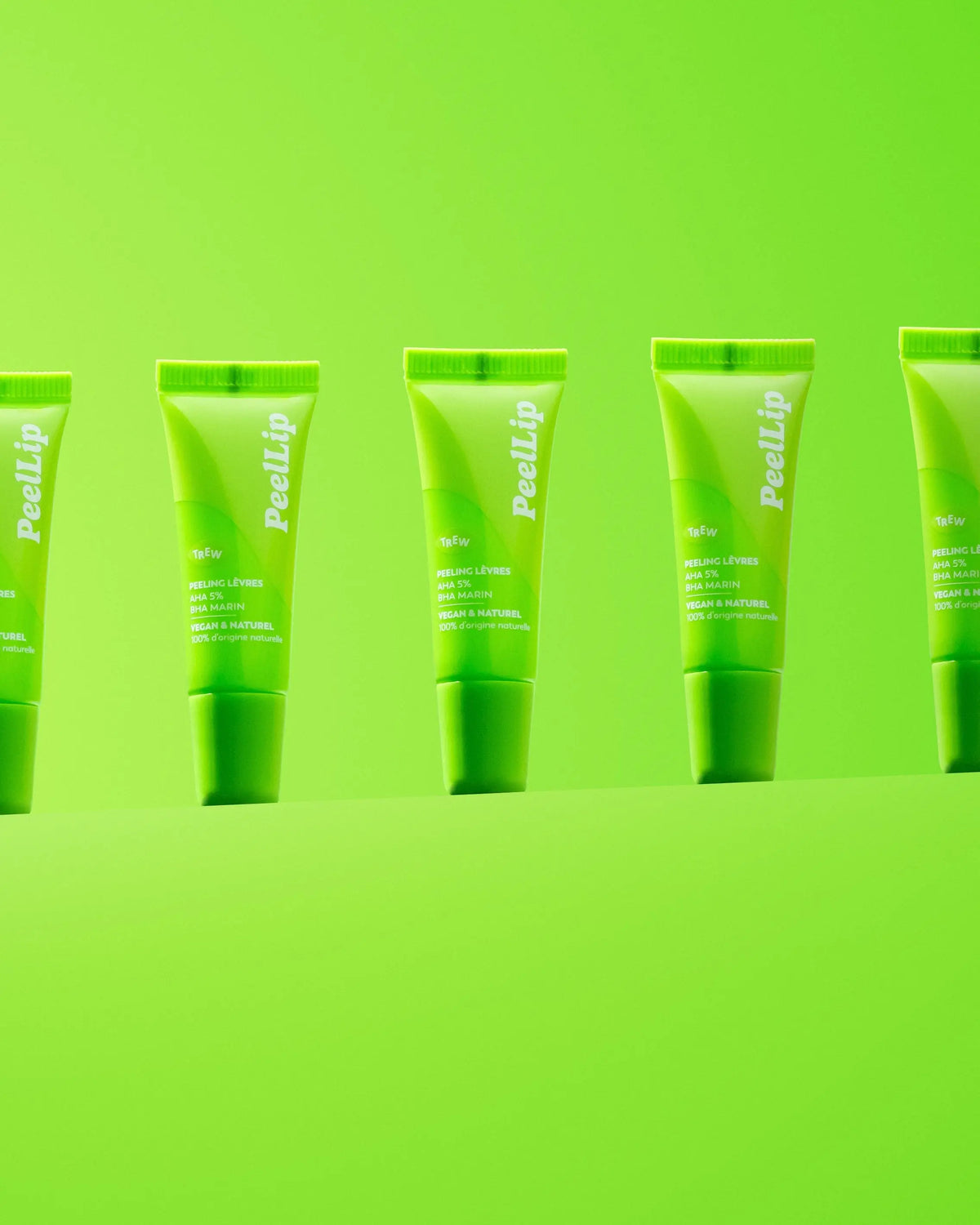 Several bright green lip exfoliant squeeze tubes standing in a row against a matching lime green background.