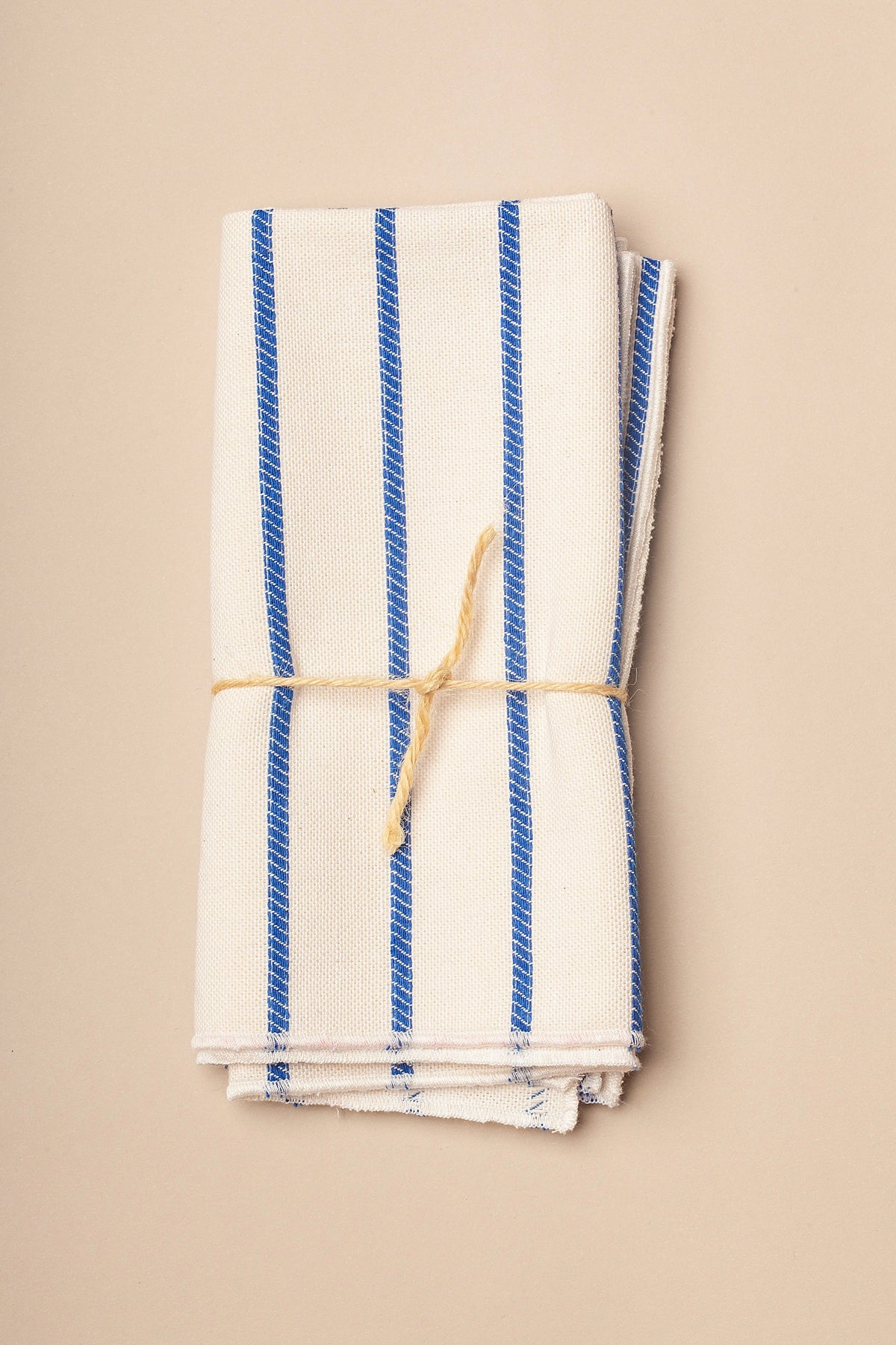 Toalla de cocina de algodón blanca con rayas azules, enrollada y atada con cuerda natural.