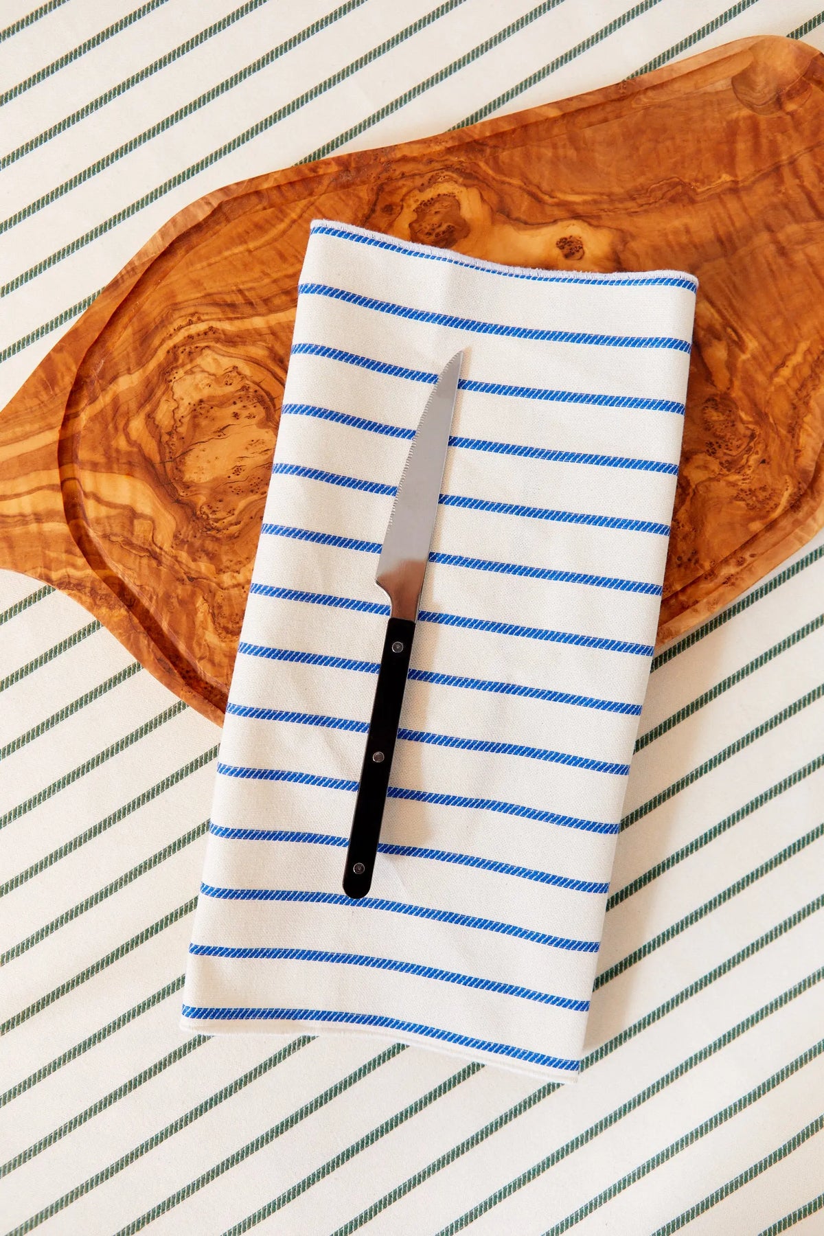Cuchillo de cocina acero inoxidable con mango negro sobre servilleta de rayas azules y blancas, fondo de madera.