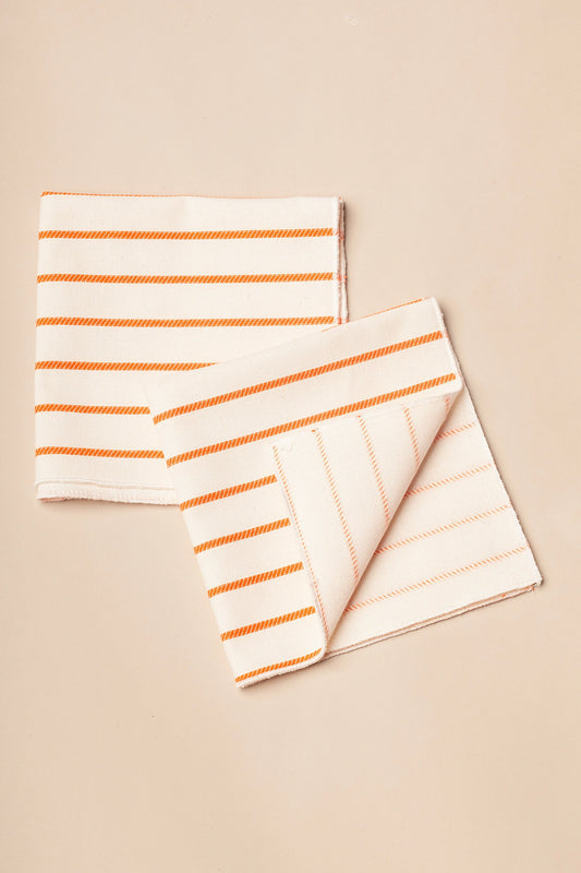 Pack de dos servilletas de tela color crema con rayas horizontales naranjas sobre fondo neutro.