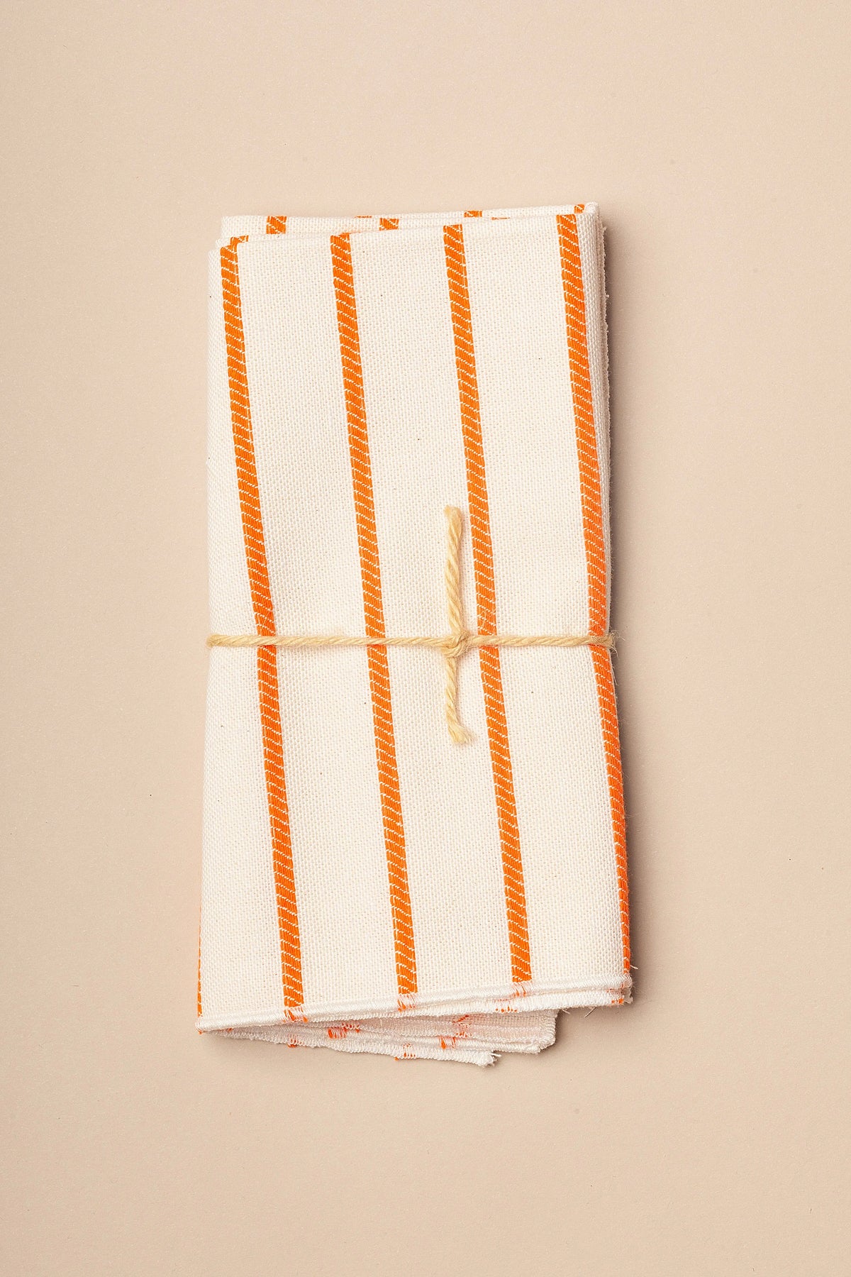 Pack de dos servilletas de tela color crema con rayas verticales naranjas, atadas con una cuerda de yute sencilla.