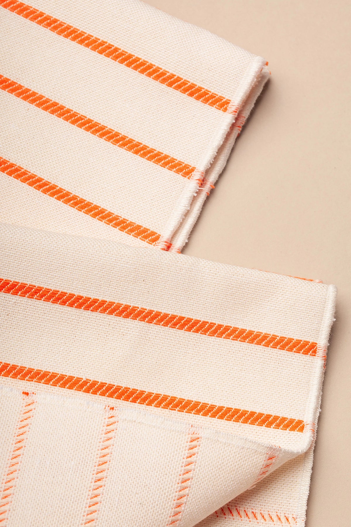 Pack de dos servilletas de tela color crema con rayas verticales tejidas en color naranja, estilo rústico y natural.