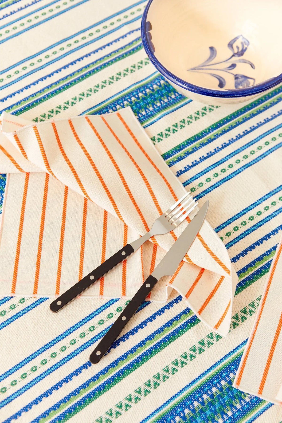 Pack de dos servilletas de tela color crema con rayas diagonales naranjas sobre un mantel con motivos geométricos.