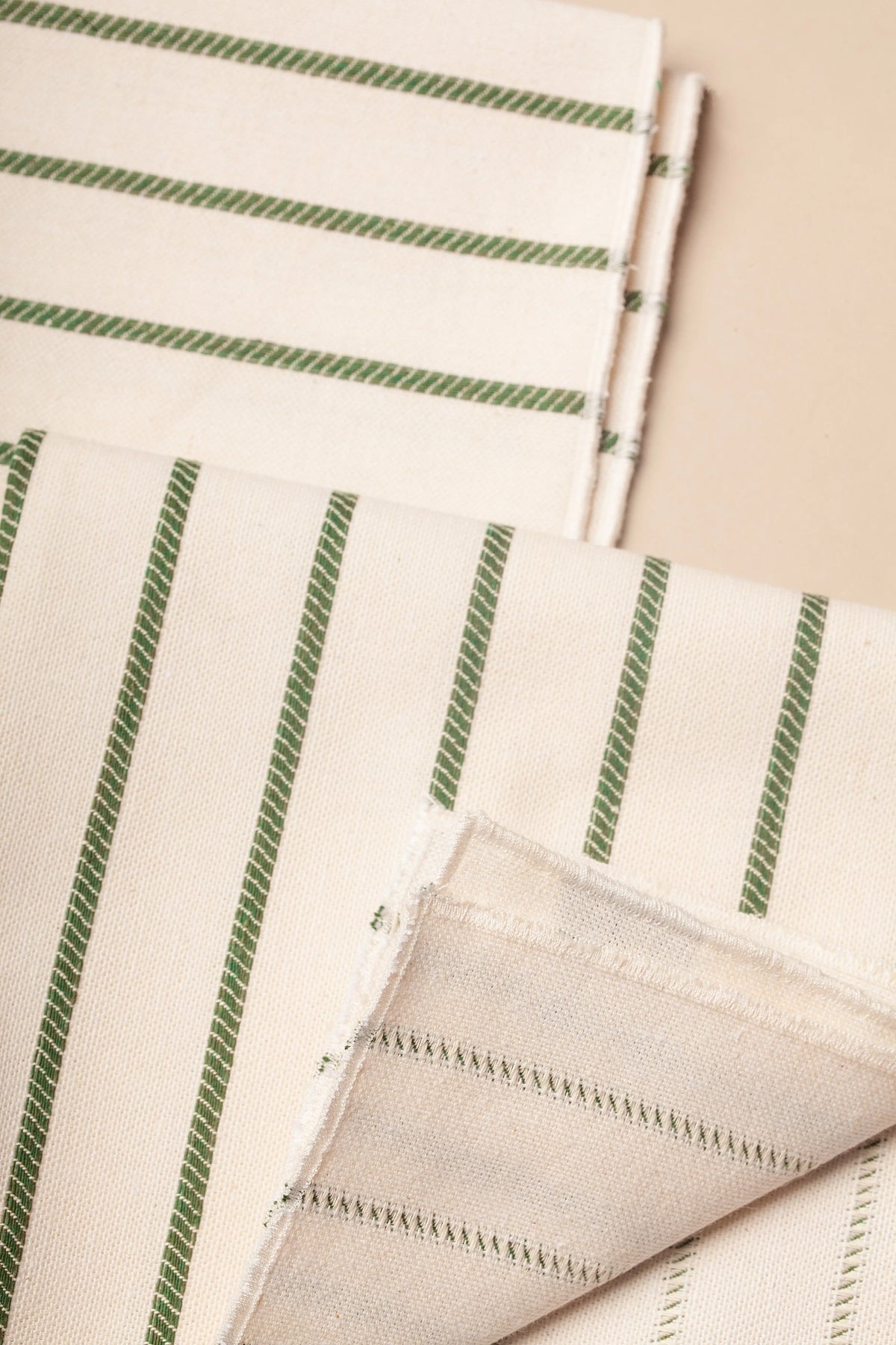 Pack de dos servilletas de tela color crudo con estampado de rayas verticales verdes en tejido de estilo rústico.