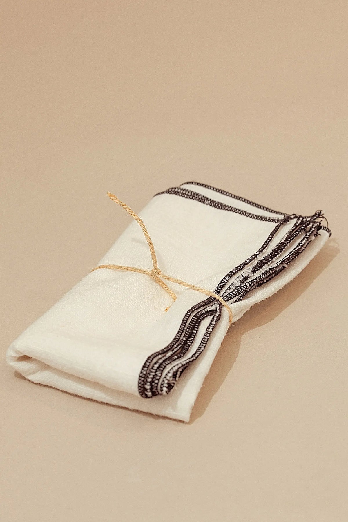 Pack de dos servilletas de lino blanco roto con borde oscuro decorativo y atadas con un cordel de fibra natural.