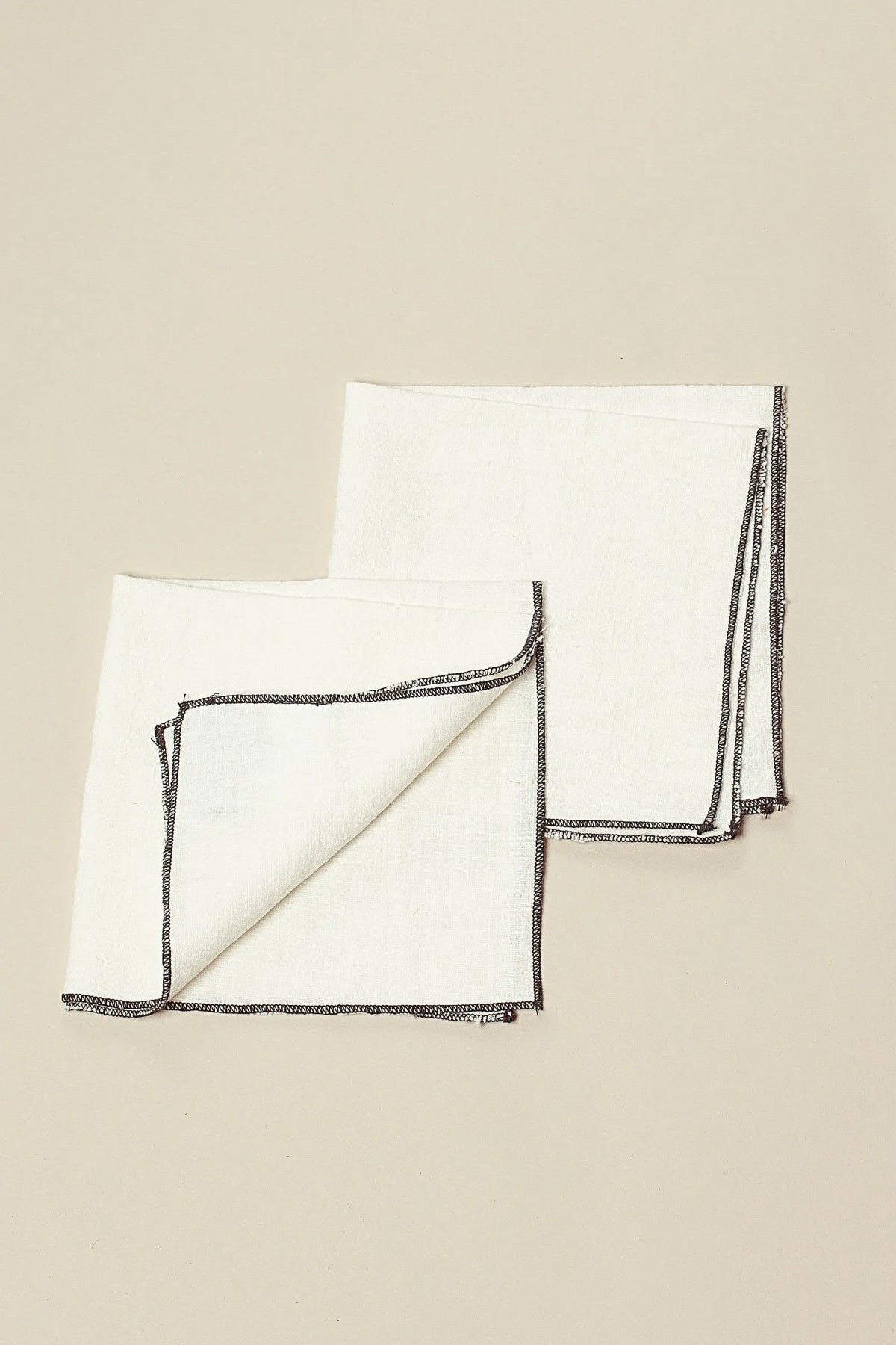 Pack de dos servilletas de lino en color blanco roto con bordes rematados en hilo oscuro de estilo artesanal.