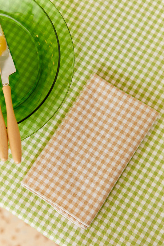 Servilleta textil de algodón con estampado de cuadros vichy beige sobre un mantel de cuadros verdes y blancos.