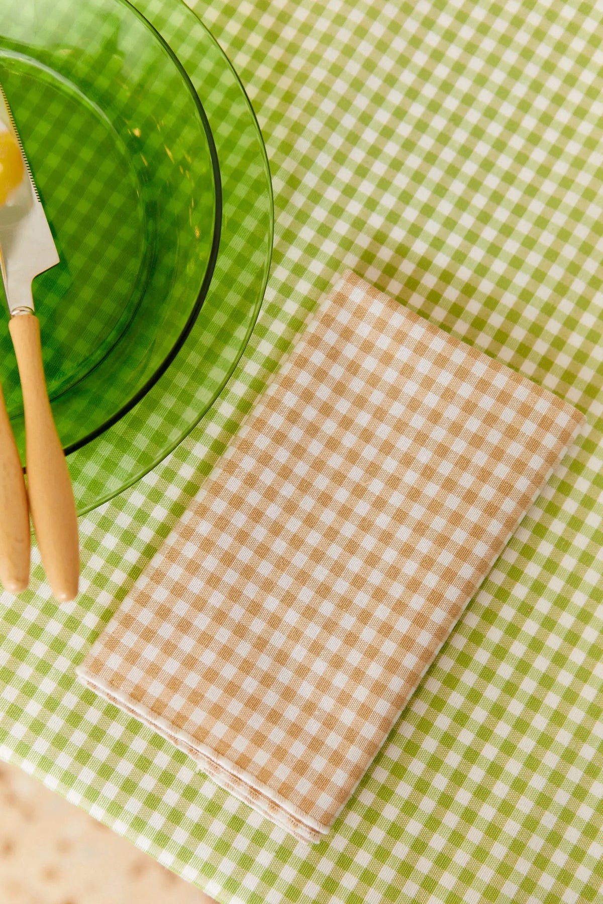 Servilleta textil de algodón con estampado de cuadros vichy beige sobre un mantel de cuadros verdes y blancos.