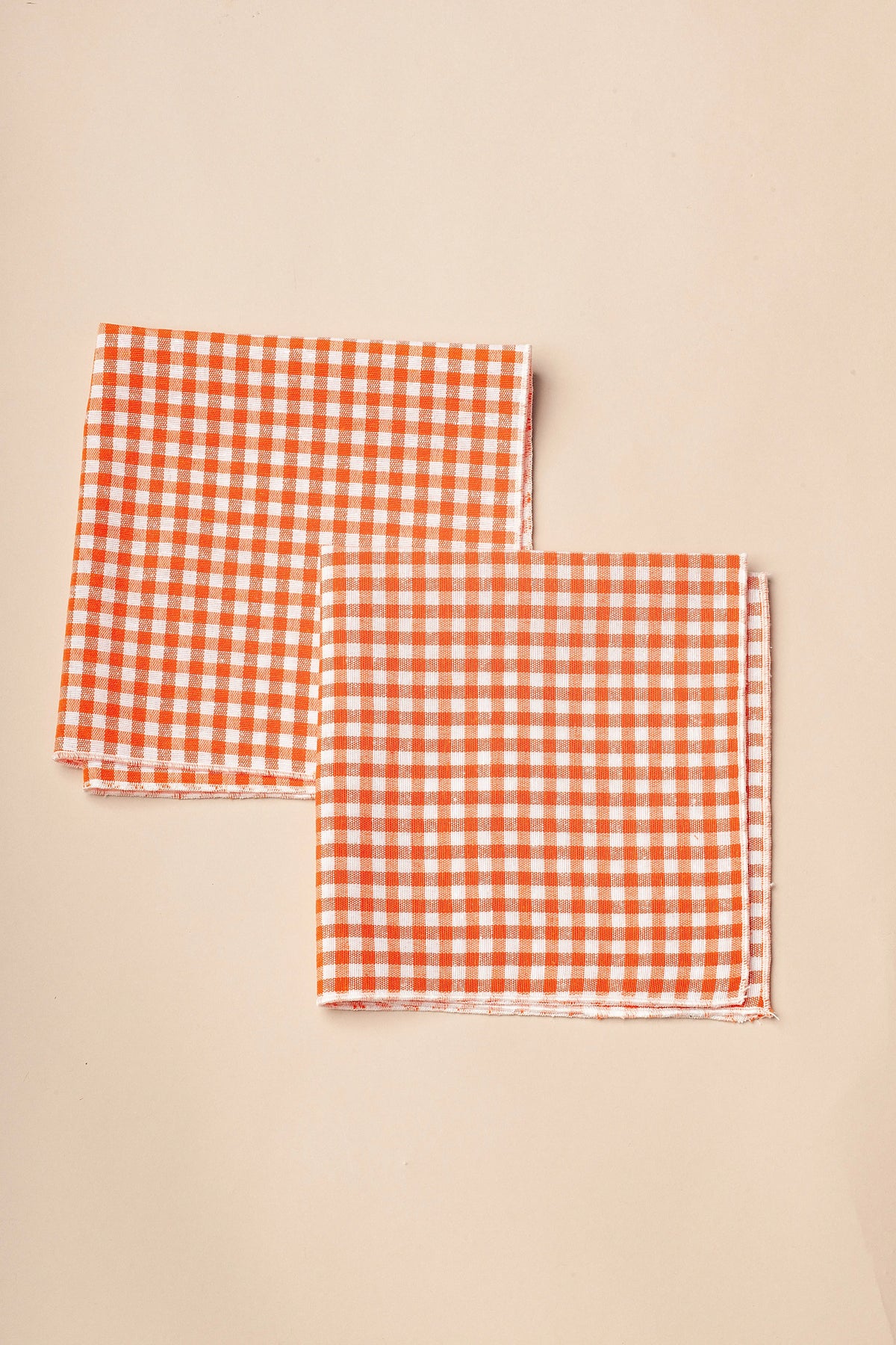 Pack de dos servilletas de tela con estampado de cuadros vichy en naranja y blanco sobre fondo beige.