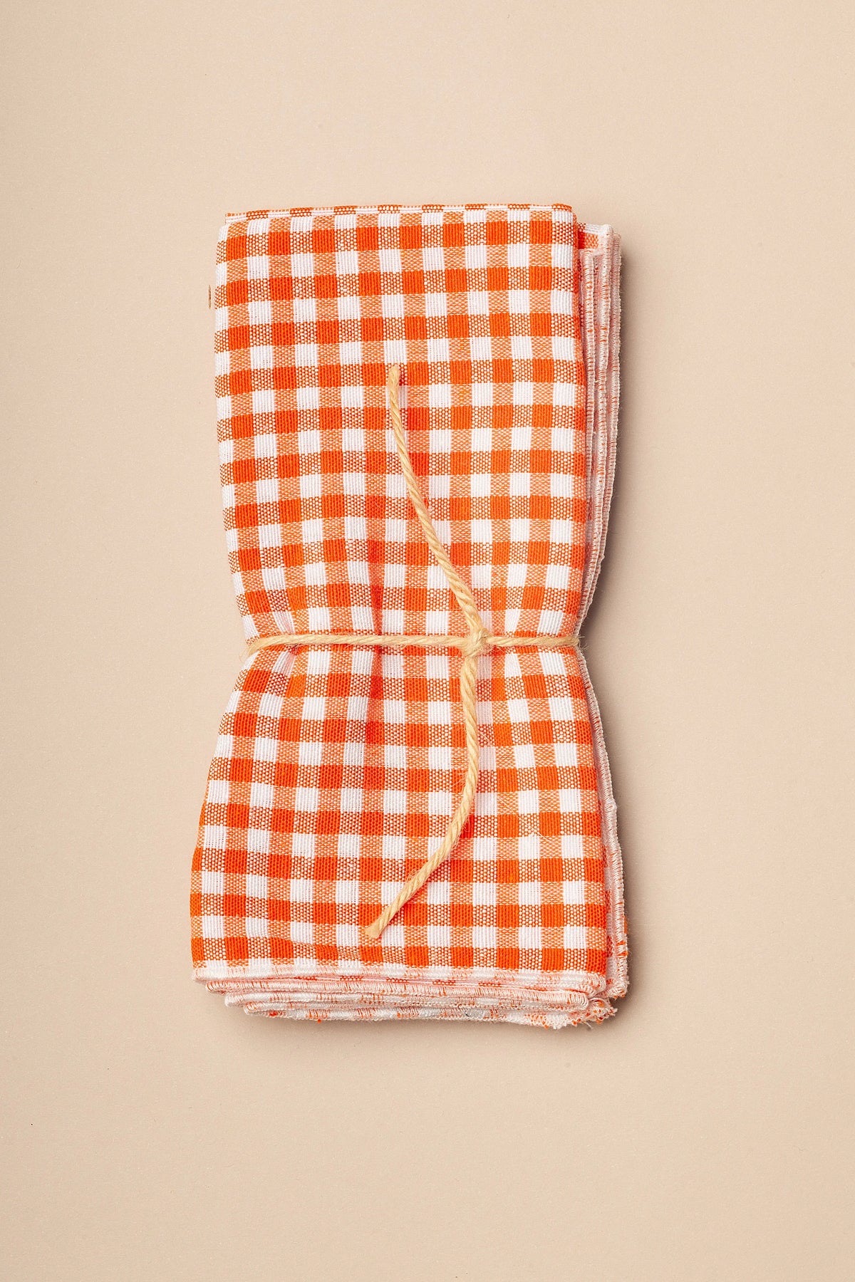 Pack de dos servilletas de tela con estampado vichy de cuadros pequeños en color naranja y blanco, atadas con cuerda.