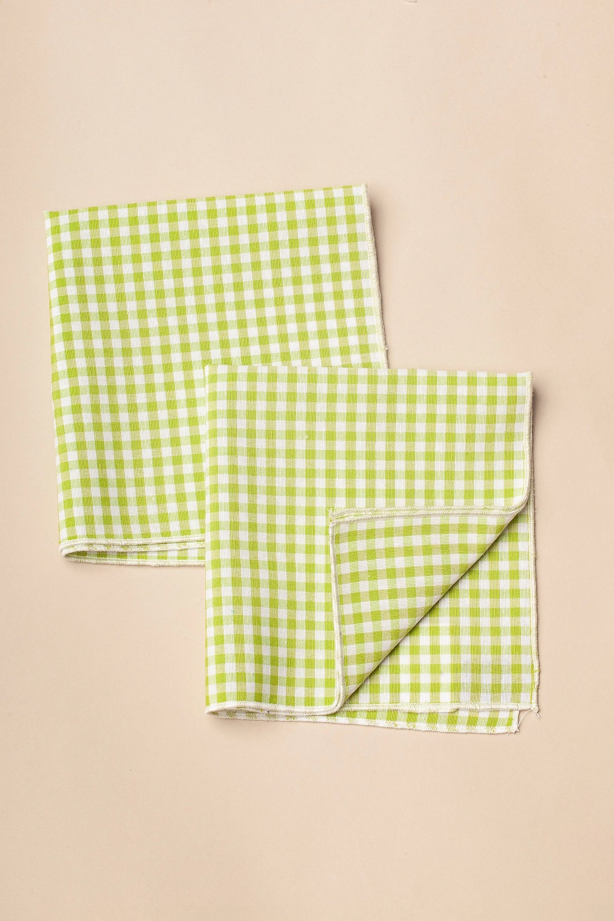 Pack de dos servilletas de tela con estampado de cuadros vichy en color verde y blanco sobre fondo beige claro.