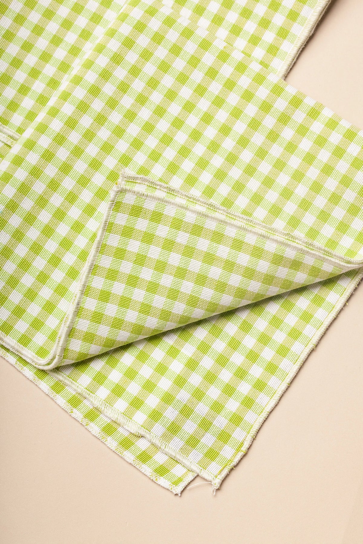 Two cloth napkins with a small lime green and white gingham check pattern and finished edges.