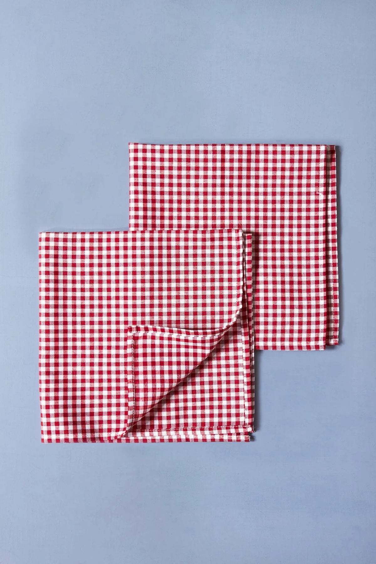 Pack de dos servilletas de tela con estampado de cuadros vichy en rojo y blanco sobre fondo azul claro.