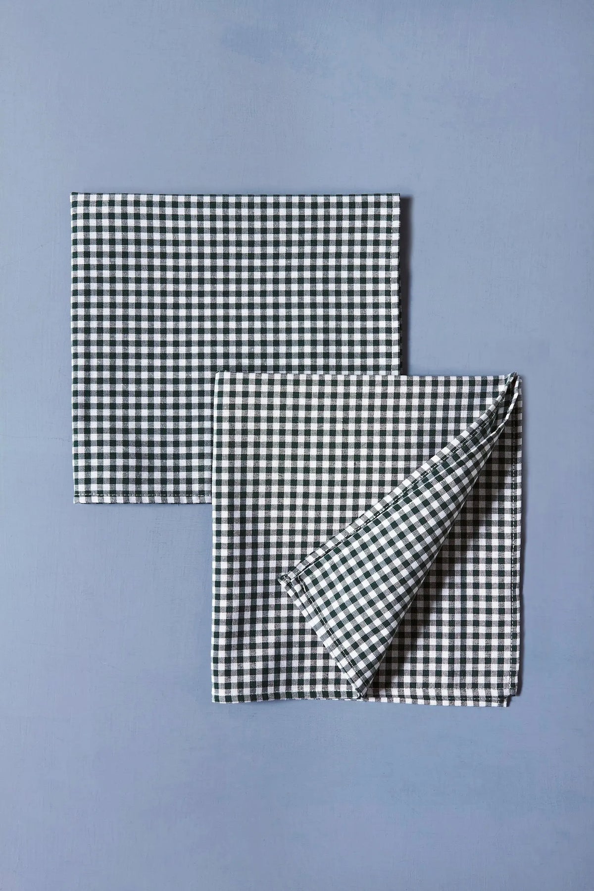Pack de dos servilletas de tela con estampado de cuadros vichy en color verde oscuro sobre fondo azul.