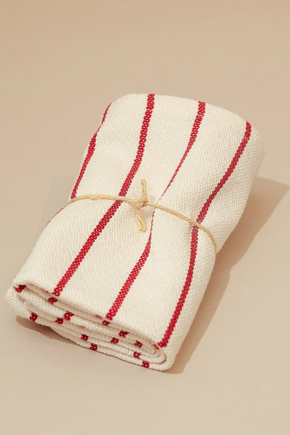 Pack de dos servilletas de loneta beige con rayas verticales granates, atadas con una cuerda de fibra natural.