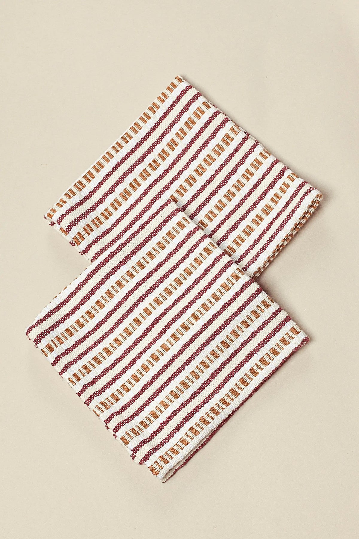 Two folded fabric napkins with cream, maroon, and tan striped, chain-link textured patterns on a beige background.