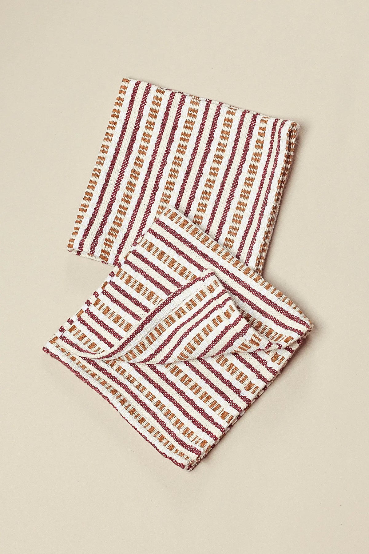 Two square cloth napkins with a cream base and textured vertical stripes in maroon and tan.