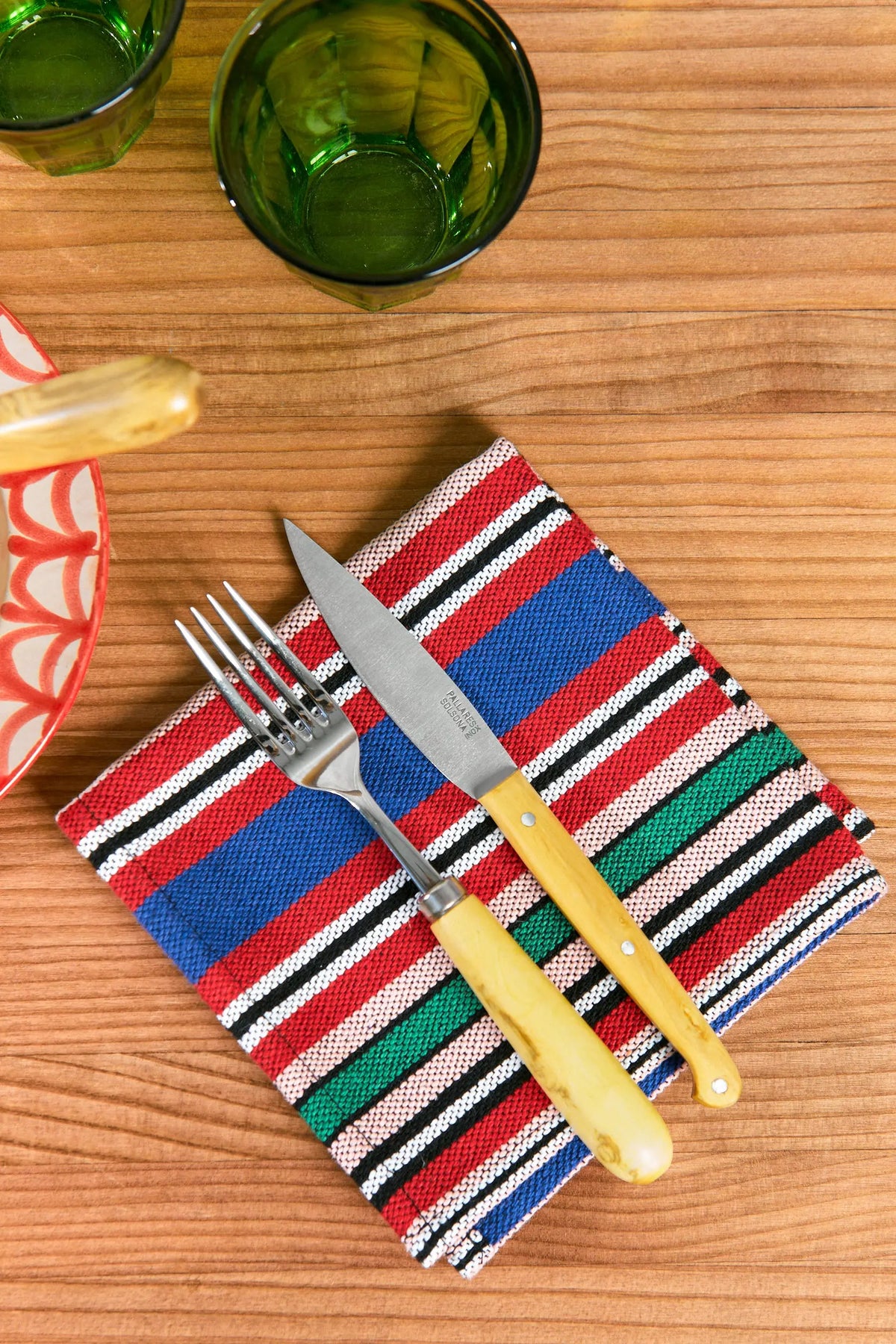 Servilleta de tela con rayas multicolores de estilo artesanal sobre mesa de madera con cubiertos encima.