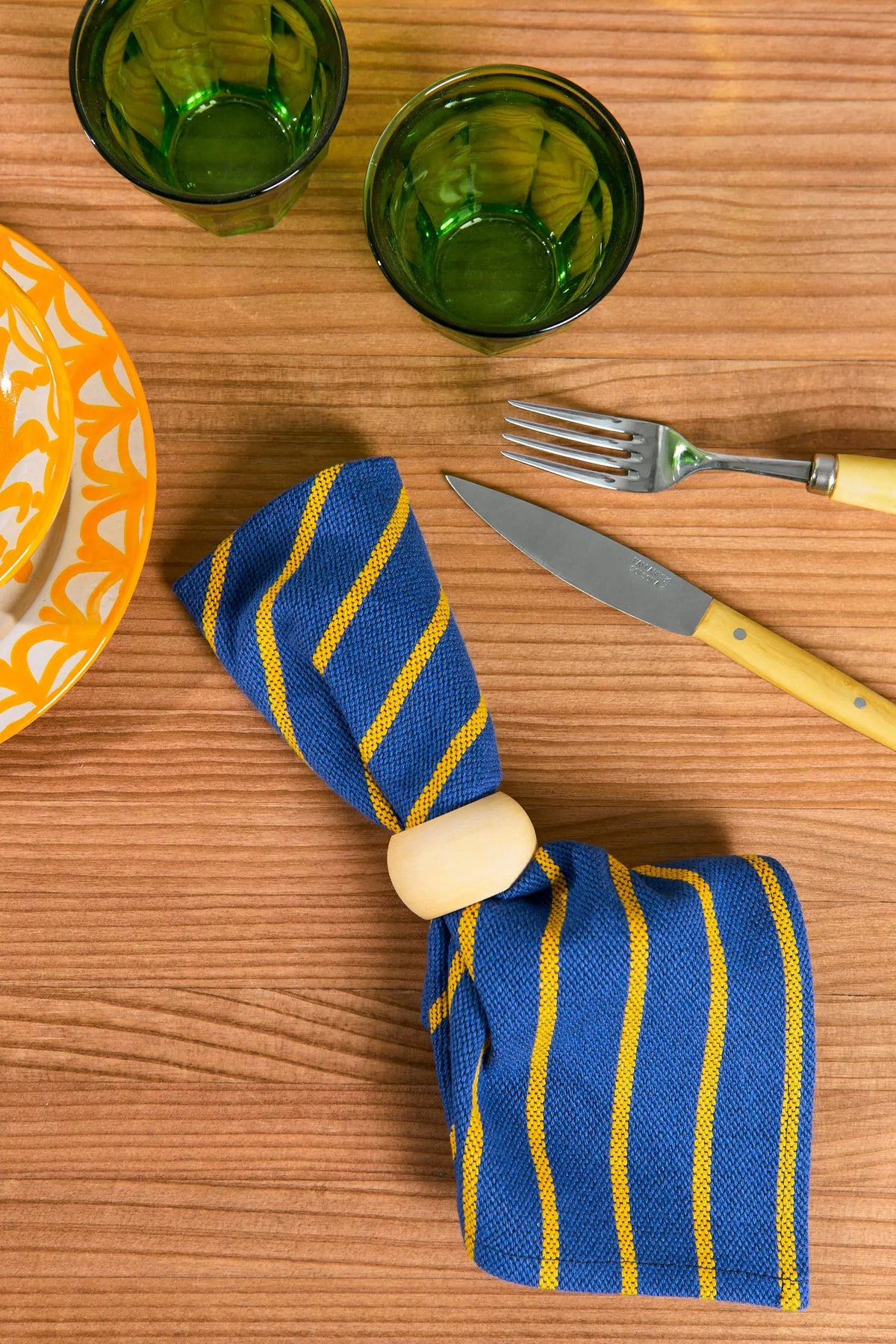 Servilleta de tela azul con rayas amarillas, sujeta por un anillo de madera sobre una mesa de madera.