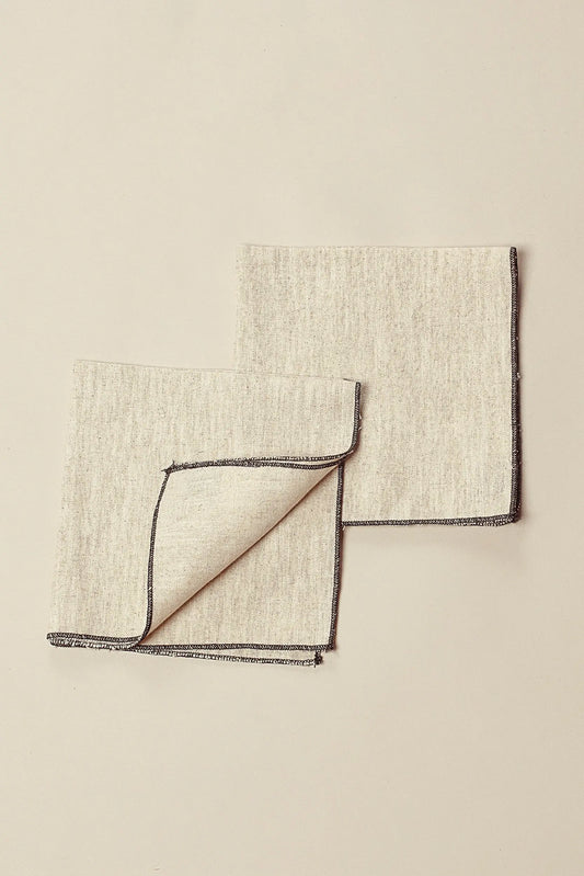 Pack de dos servilletas de lino beige, cuadradas, con acabado de costura en contraste oscuro en los bordes.