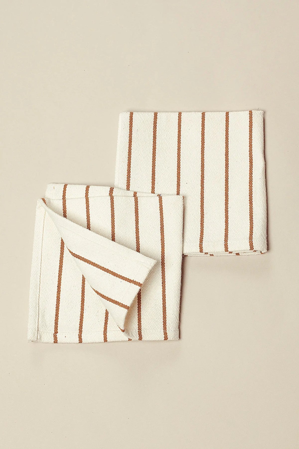 Pack de dos servilletas de loneta en color crema con rayas verticales finas en tono caramelo, estilo natural.