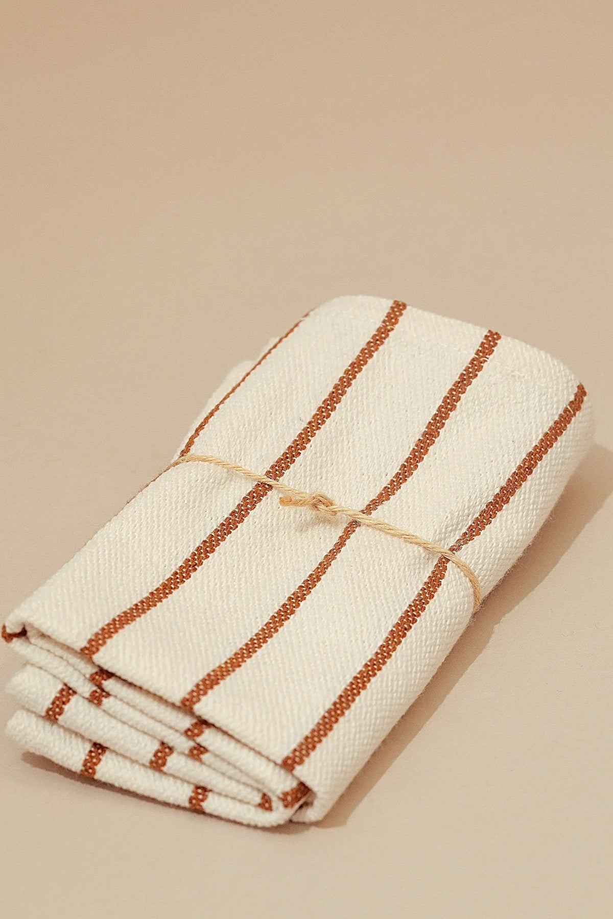 Pack de dos servilletas de loneta color crema con rayas verticales en tono caramelo, atadas con una cuerda rústica.