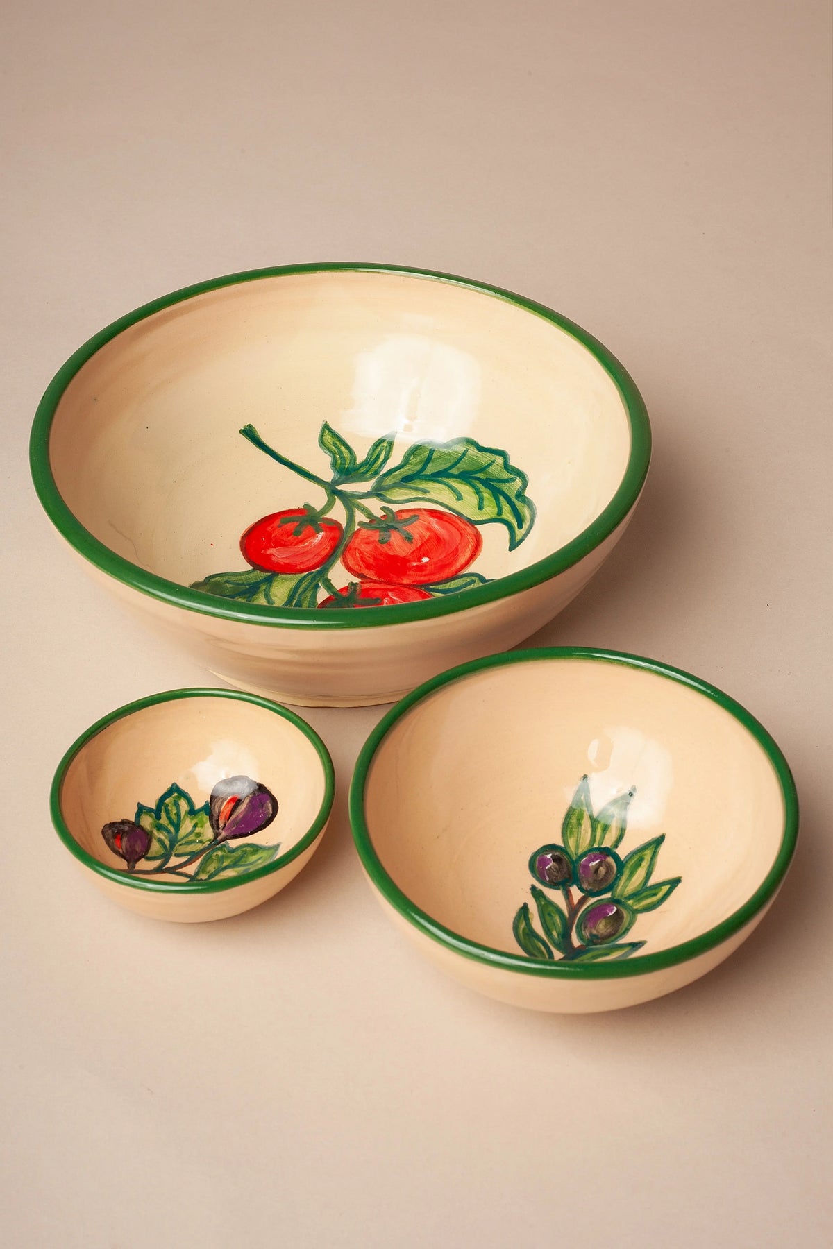 Set de tres cuencos de cerámica color crema con borde verde y motivos pintados de tomates, higos y aceitunas.