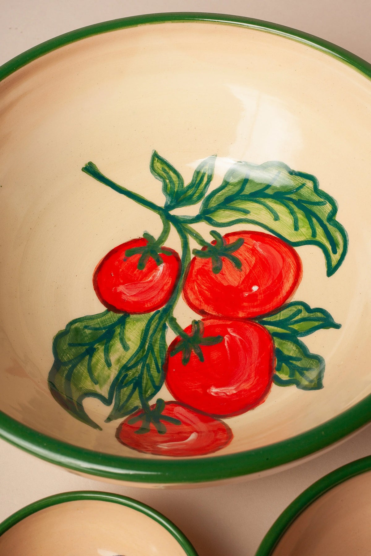 Cuenco de cerámica color crema con estampado artesanal de tomates rojos y hojas verdes, borde pintado en verde.