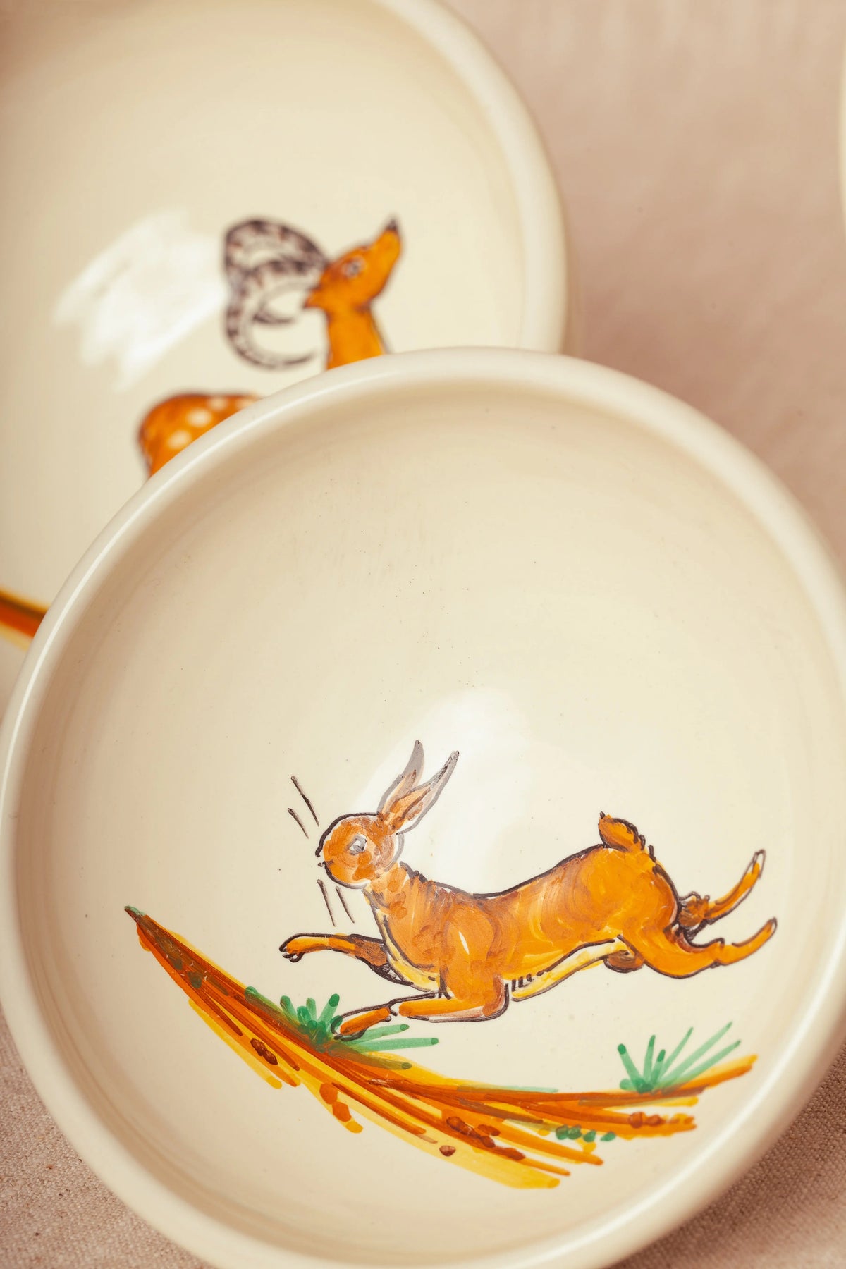 Set de dos cuencos de cerámica color crema pintados a mano con ilustraciones de estilo rústico de una liebre y un ciervo.
