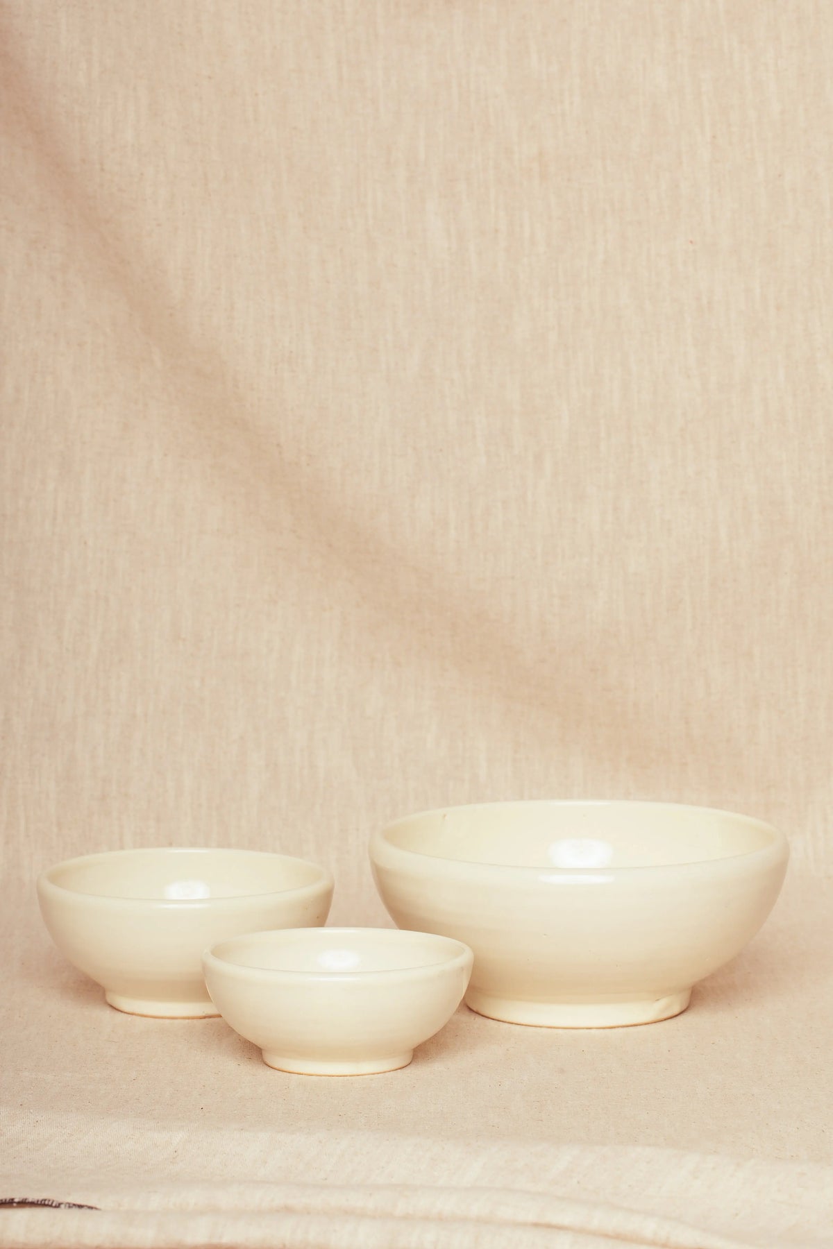 Set de tres cuencos de cerámica artesanal en color crema con diseño minimalista sobre fondo de tela rústica.
