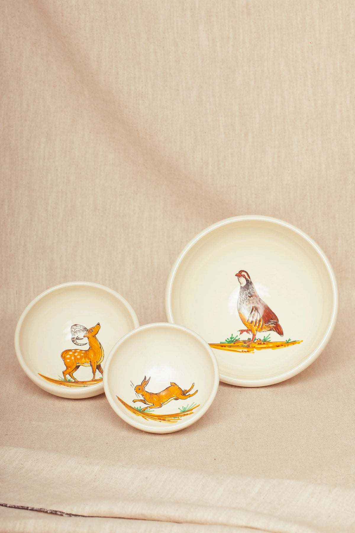Set de tres cuencos de cerámica color crema con ilustraciones pintadas de estilo rústico de una perdiz, liebre y ciervo.