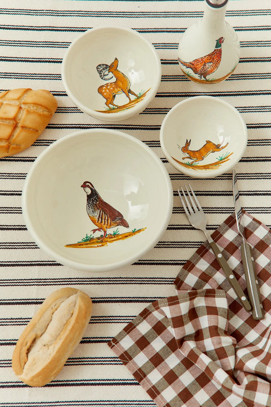Set de cuencos de cerámica color crema con ilustraciones pintadas de animales, estilo rústico sobre mantel a rayas.