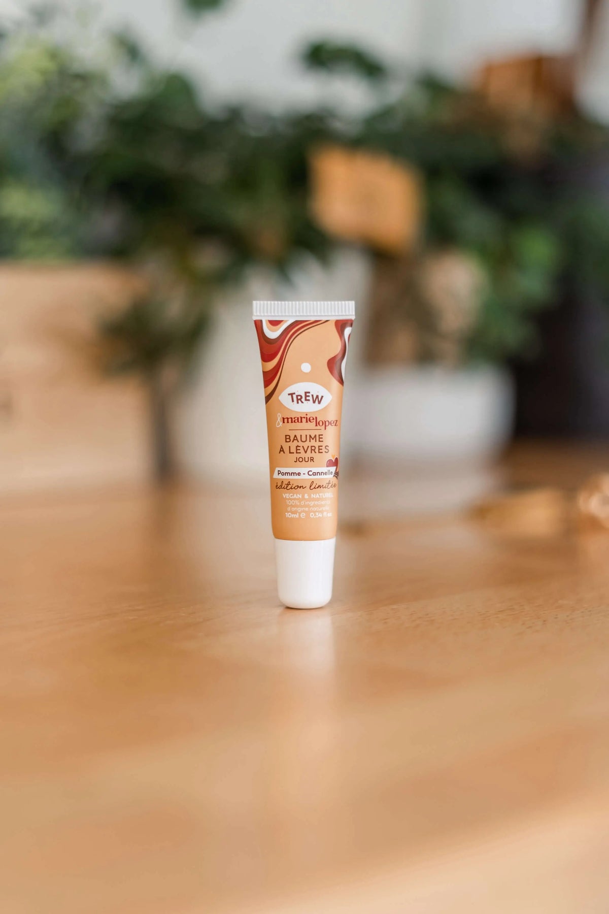 A small tan lip balm tube with a wavy brown design, standing upright on a wooden surface against a blurred backdrop.
