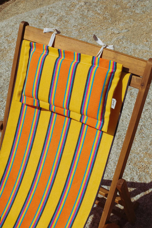 Tejido de lona para hamaca y cojín a juego con rayas verticales amarillas, naranjas y azules sobre silla de madera.