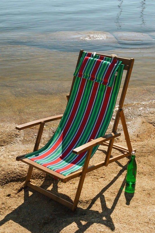 Hamaca de madera con tejido de lona a rayas rojas, verdes y blancas y cojín a juego en una playa soleada.