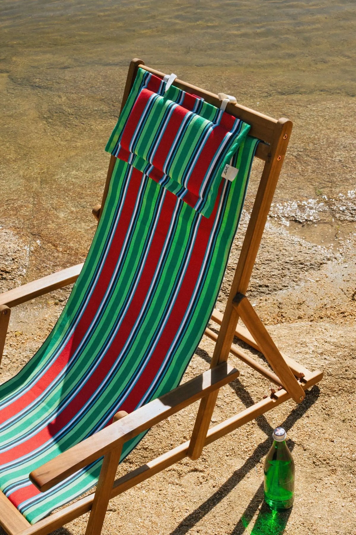Hamaca de madera con tejido de lona a rayas rojas, verdes y azules, incluyendo un cojín reposacabezas a juego.