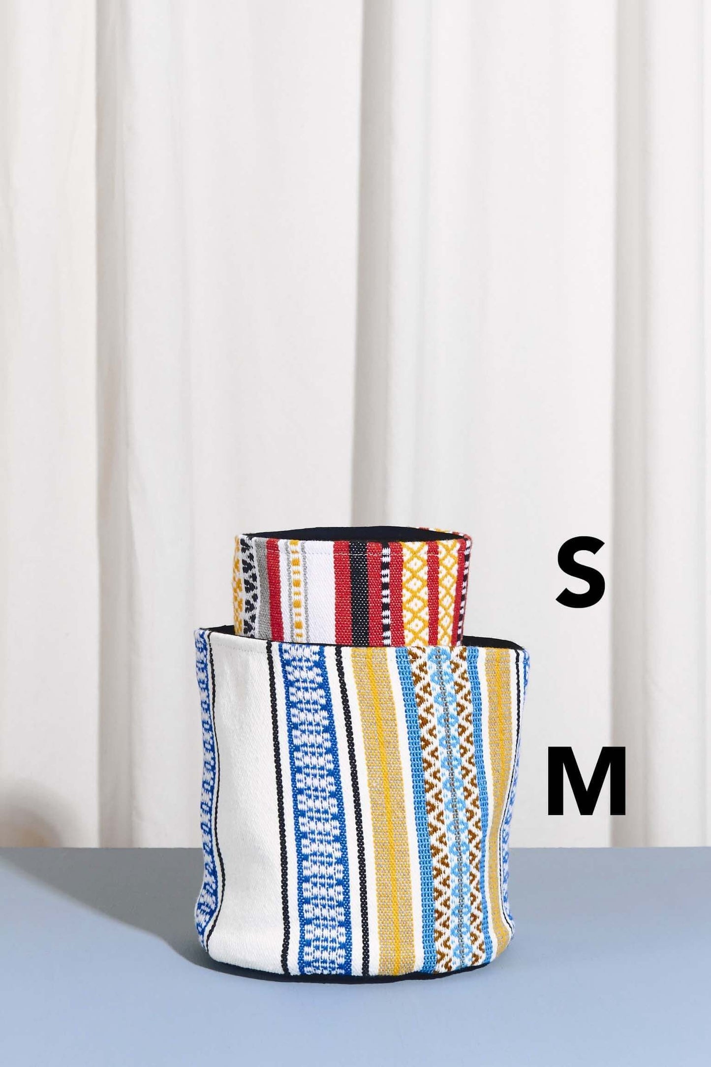 Two artisanal fabric baskets in medium and small sizes, featuring colorful geometric striped patterns.