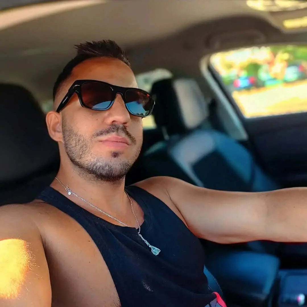 Hombre con gafas de sol retro de montura negra y lentes marrones conduciendo coche, estilo casual.