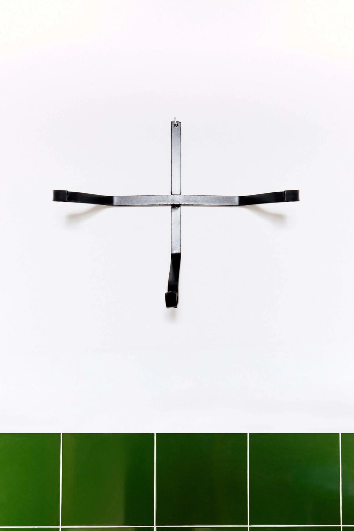Soporte de pared de hierro negro en forma de cruz, estilo minimalista industrial, diseñado para colgar lebrillos.