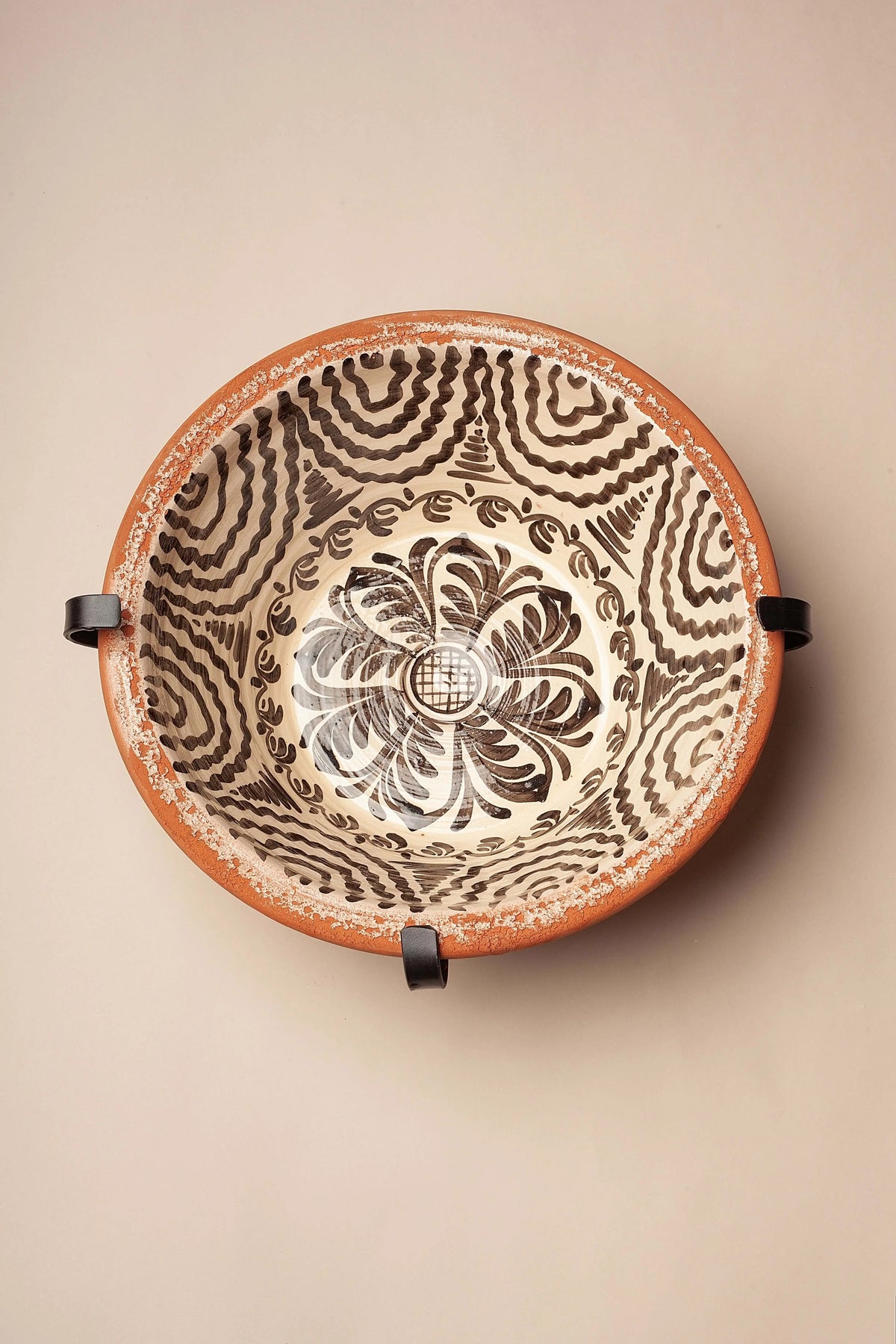 Black iron metal wall mount bracket holding a decorative, hand-painted terracotta bowl with dark brown floral motif.