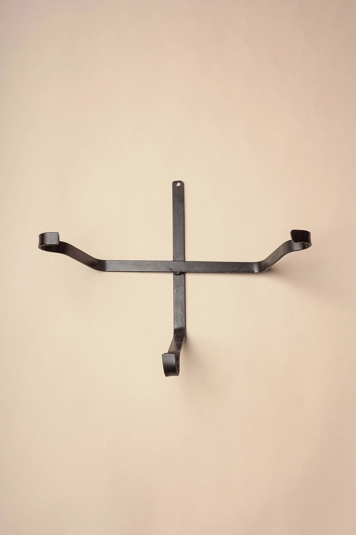 Black iron wall-mount holder with a cross design, featuring curved hooks for displaying basins or bowls.