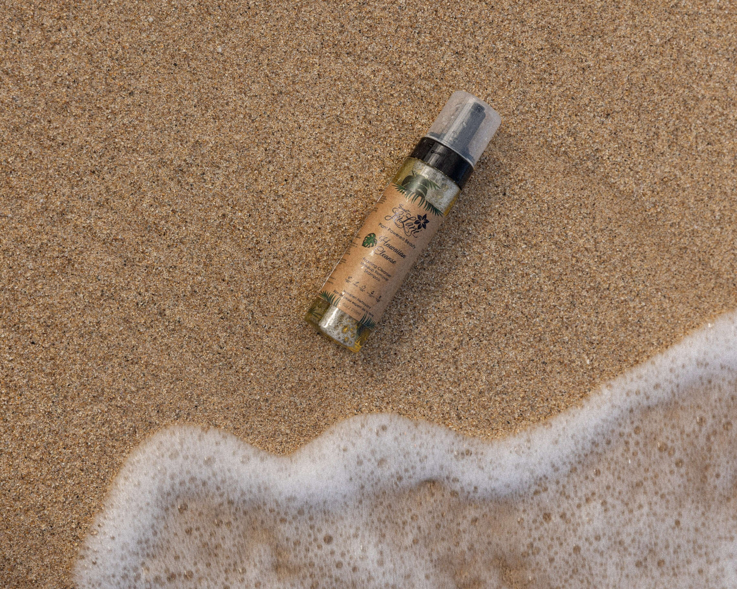 Hawaiian Cleanser spray bottle on wet sand, positioned next to a gentle incoming ocean wave with sea foam.