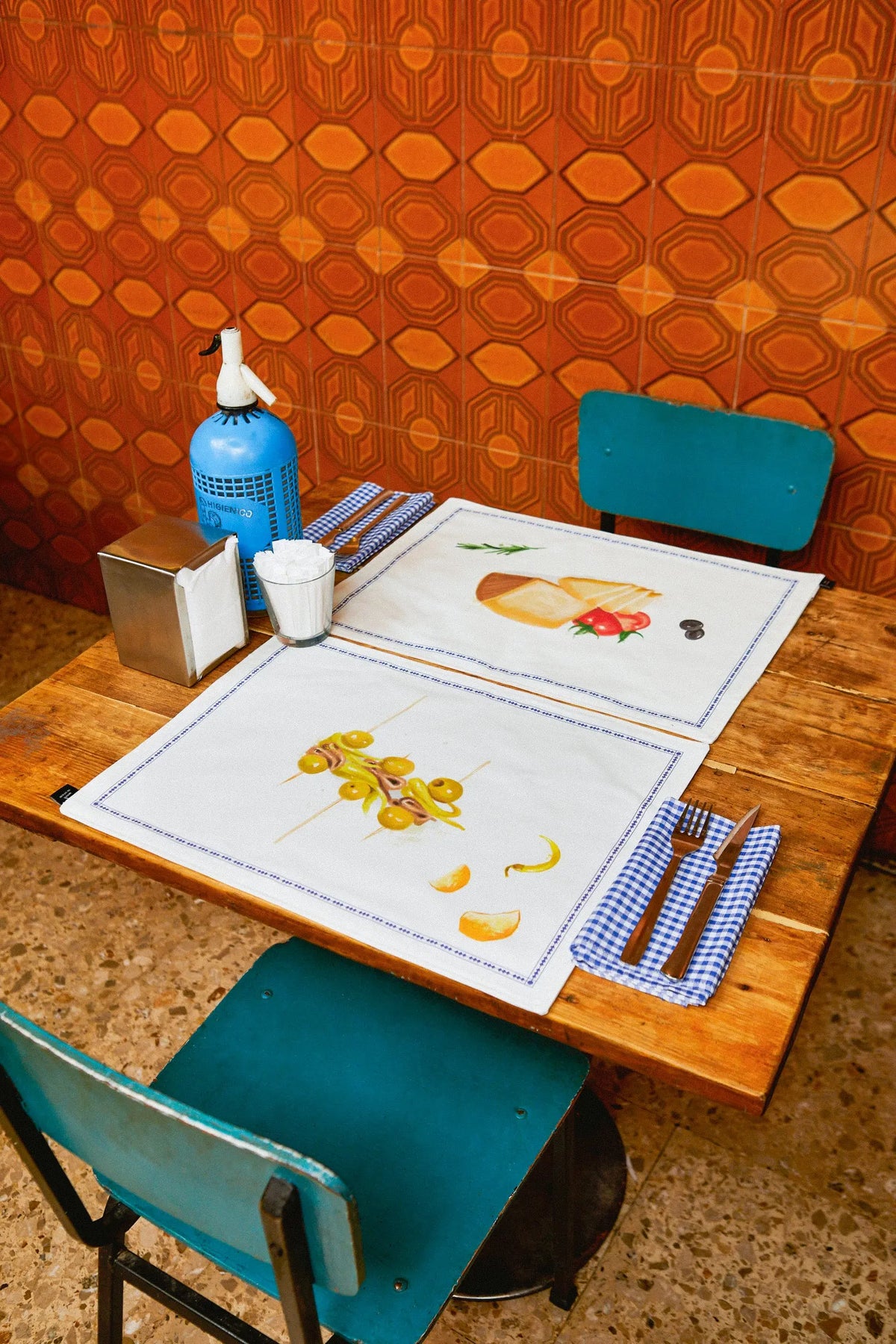 Pack de 2 manteles individuales de tela blanca con ilustraciones de tapas, ribete azul y diseño reversible.