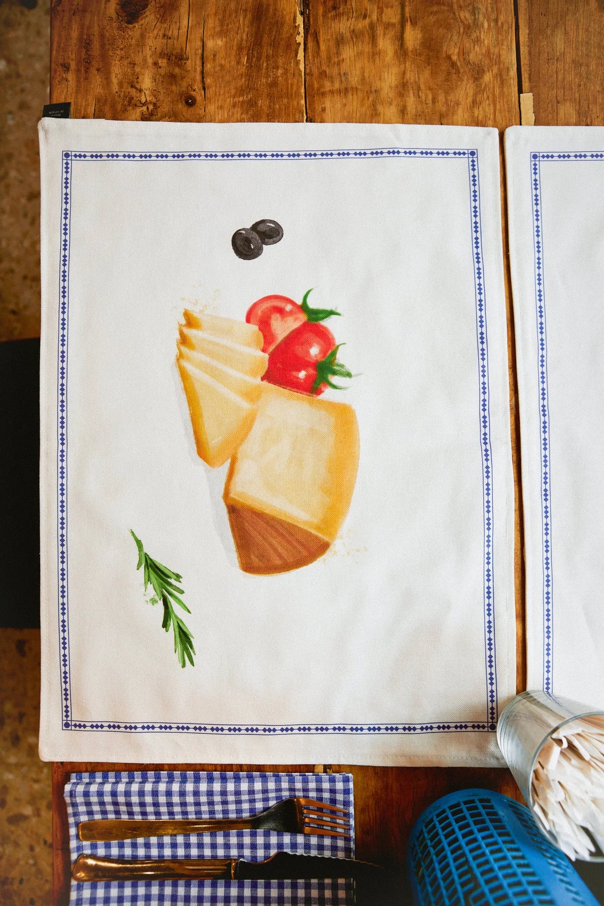 Pack de manteles individuales de tela blanca con ilustración de tapas, borde geométrico azul y estilo rústico reversible.