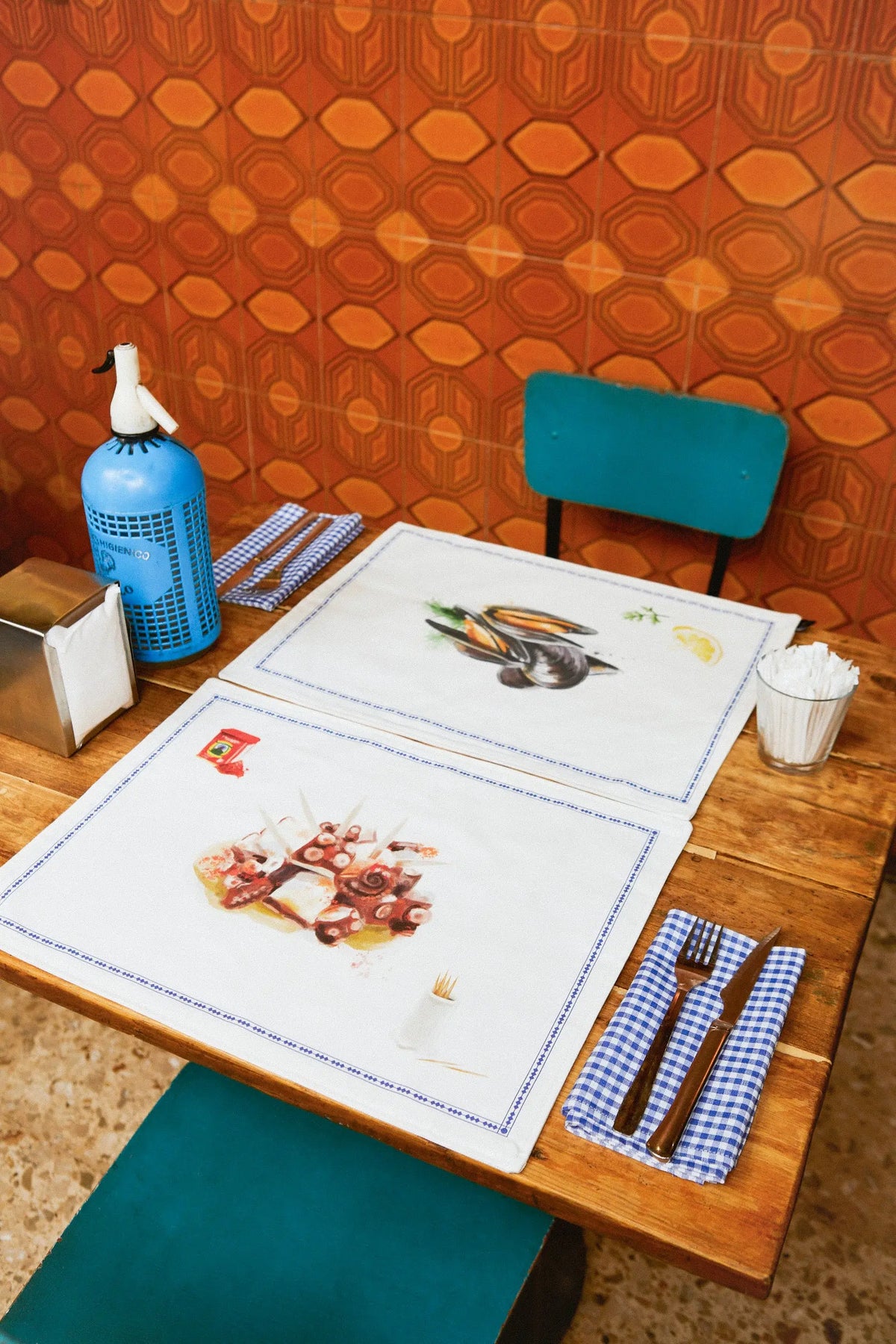 Pack de 2 manteles individuales reversibles blancos con ilustraciones de tapas de mar en una mesa de madera.