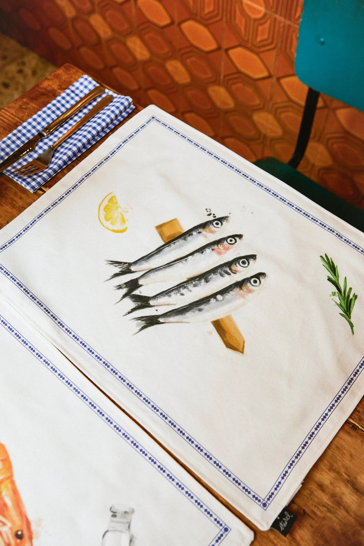 Pack de 2 manteles individuales reversibles con estampado de sardinas, limón y romero sobre fondo blanco.