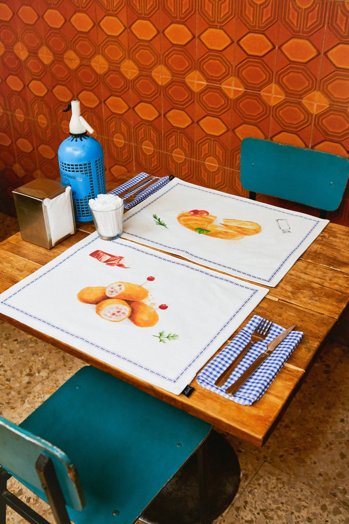 Pack de 2 manteles individuales reversibles con estampado de tapas españolas, diseño textil sobre mesa de madera.