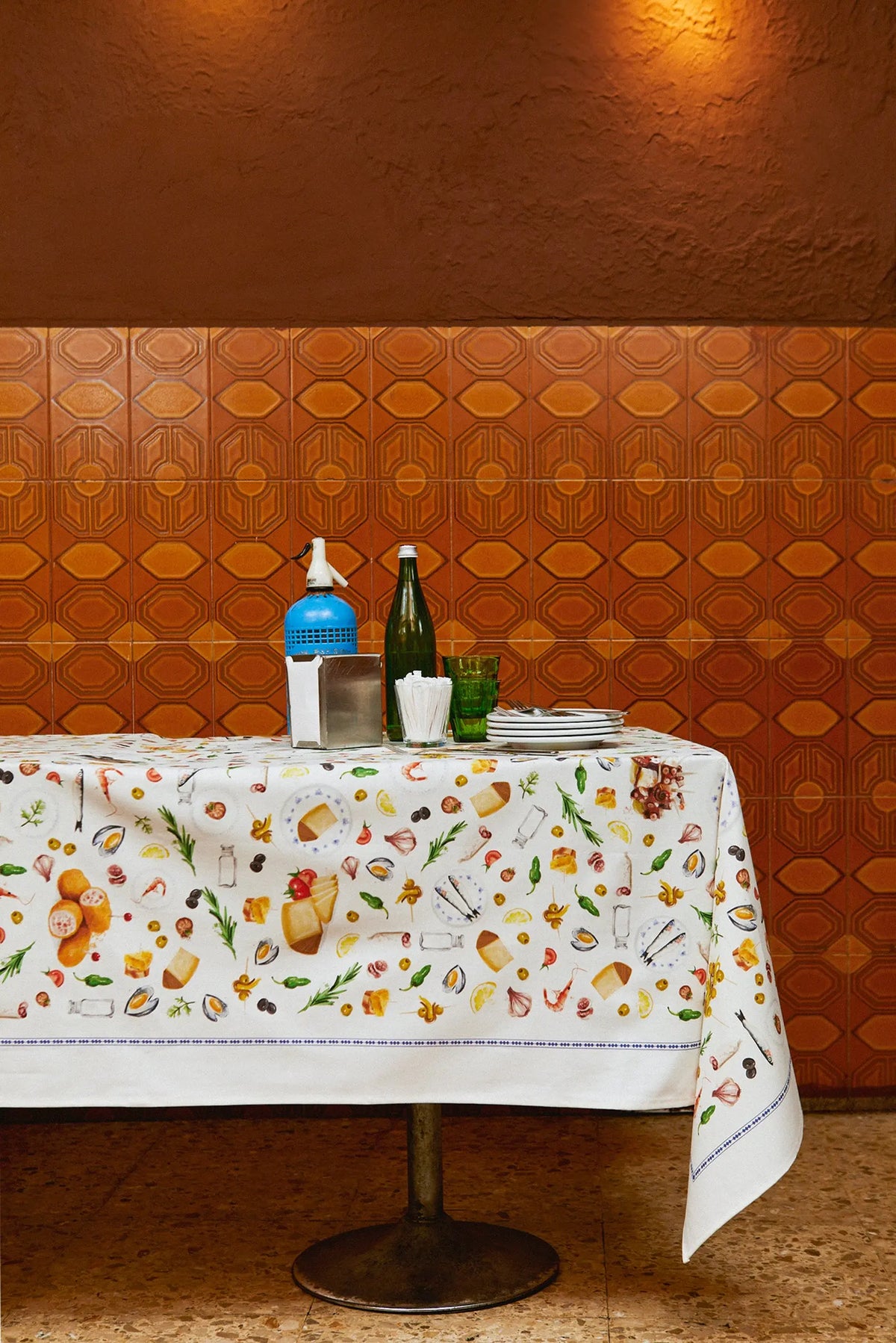 Mantel blanco de tela con estampado de ilustraciones coloridas de tapas españolas y borde con finas líneas azules.